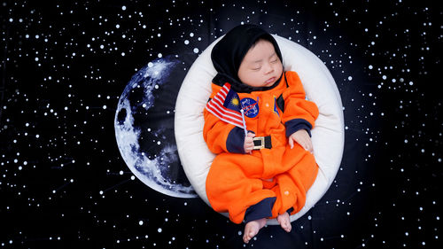 Digital composite image of boy wearing space suit while sleeping on bed against moon