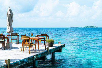 Chairs and table by sea against sky