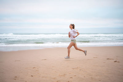 Rear view of woman standing at beach against sky