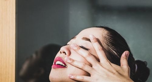 Close-up of young woman touching face by window