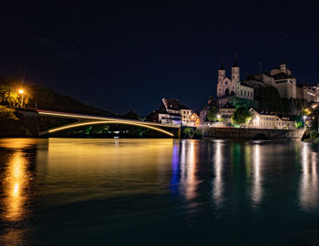 Illuminated bridge over river against buildings at night