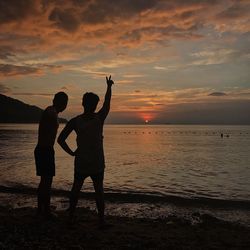 Fiends standing on shore against cloudy sky during sunset