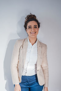 Smiling businesswoman wearing blazer in front of wall