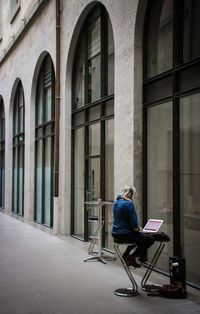 Rear view of woman sitting on chair against building