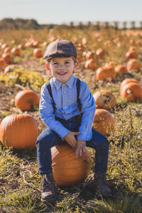 Portrait of smiling boy sitting on pumpkin at field