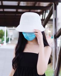 Young woman wearing mask sand hat standing outdoors