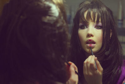 Woman applying lip gloss reflecting on mirror