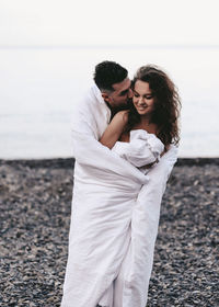 A diverse of lovers a man and a woman embrace under a blanket on the ocean at night outdoor