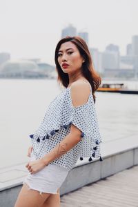 Portrait of young woman standing against river in city