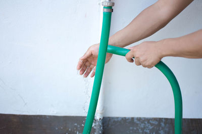 Close-up of woman washing hand with pipe against wall