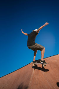 Low section of person jumping against clear blue sky