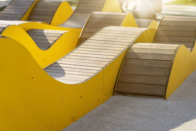 Modern yellow curved wooden benches for relaxing in city park on sunny day. public city resting area