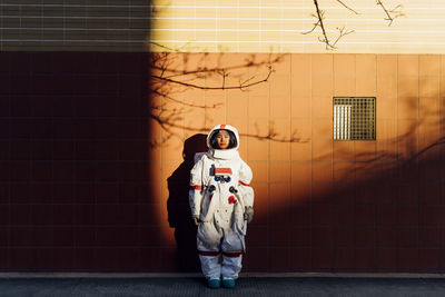 Woman astronaut in space suit standing by wall during sunset