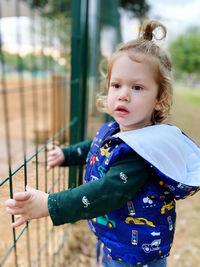 Portrait of cute baby boy standing outdoors holding a fence 