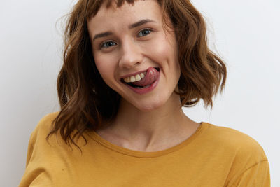 Smiling young woman sticking out tongue against white background