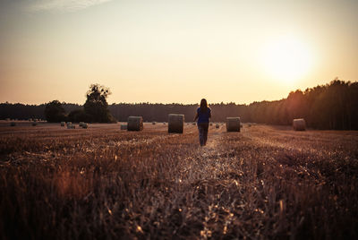 Rear view of woman standing on field against sky during sunset