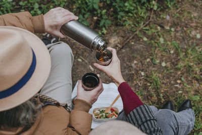 Man pouring hot tea from thermos to woman in forest