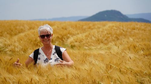 Woman wearing sunglasses on barley field against sky