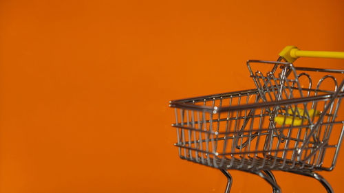 Close-up of shopping cart against yellow background