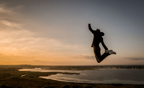 Silhouette man jumping over sea against sky