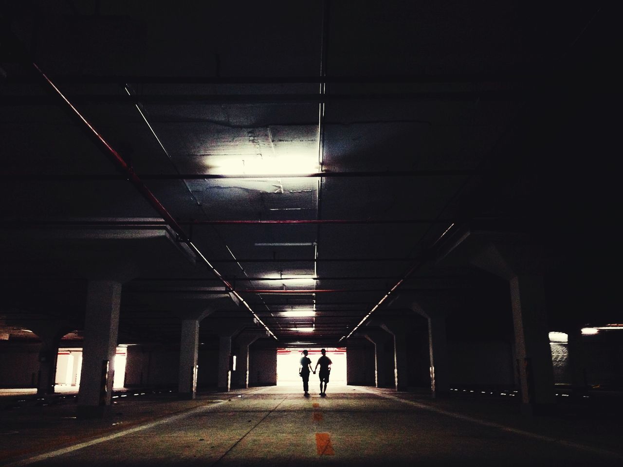 illuminated, indoors, men, walking, lifestyles, the way forward, rear view, full length, person, night, built structure, architecture, silhouette, leisure activity, tunnel, lighting equipment, diminishing perspective