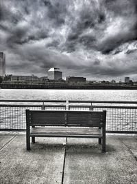 Empty bench overlooking calm river with buildings in background