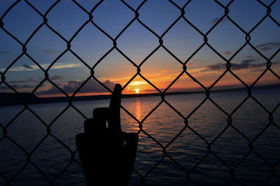 Close-up of silhouette hand by sea against sky during sunset