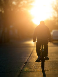 Rear view of silhouette man walking on street against sky during sunset