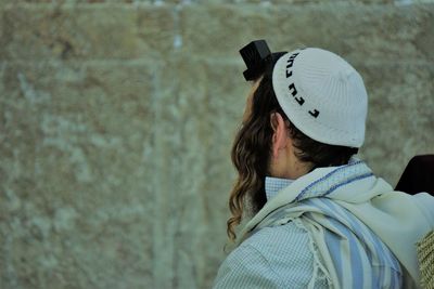 Rear view of man wearing hat and tefillin against wall
