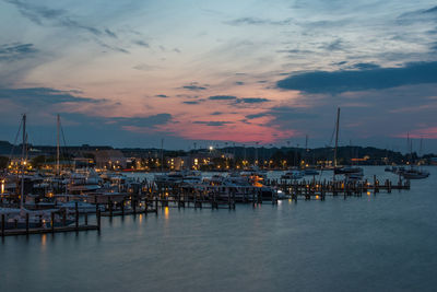 Sailboats moored in harbor at sunset