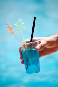 Close-up of hand holding drink against blue sky