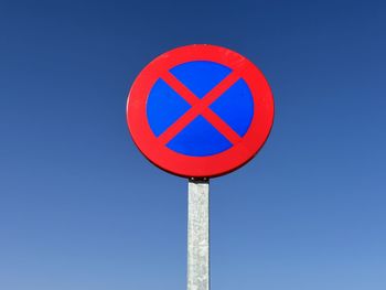 Low angle view of road sign against clear blue sky