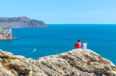 People on cliff by sea against clear blue sky