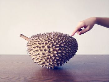 Cropped image of hand touching durian fruit on table against gray background