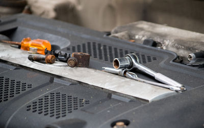 Various mechanical tools are laid out on the top of an engine, as a mechanic works under the hood