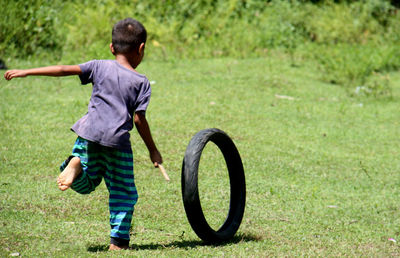 Rear view of boy playing with tire on field