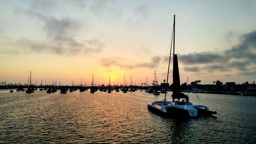 Sailboat on sea by harbor against sky during sunset