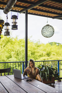 Focused young female in casual summer dress browsing smartphone while sitting at table on outdoor restaurant terrace