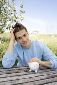 Portrait of young woman holding piggy bank on table