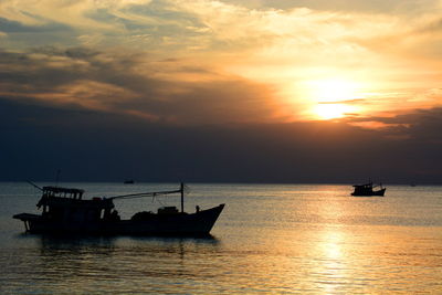 Silhouette boats sailing in sea against cloudy sky during sunset