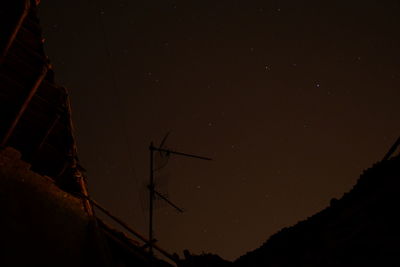 Low angle view of silhouette electricity pylons against sky at night