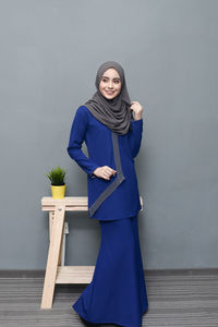 Portrait of smiling young woman standing against blue wall