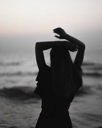 Silhouette woman standing at beach against sky during sunset