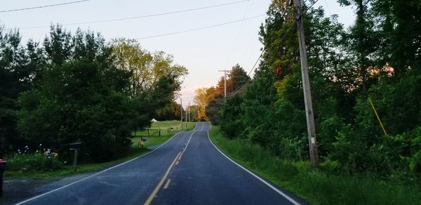 Empty road amidst trees against sky