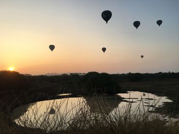 Hot air balloons flying over lake against sky during sunset