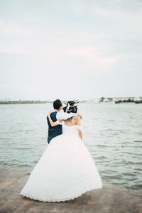 Bride and groom standing on pier by sea against sky