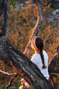 Rear view of woman sitting on tree trunk