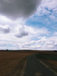 Road by agricultural field against sky