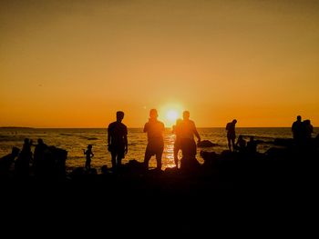 Silhouette people on beach against sky during sunset