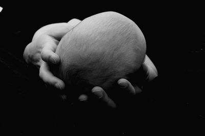 Close-up of hands holding baby against black background